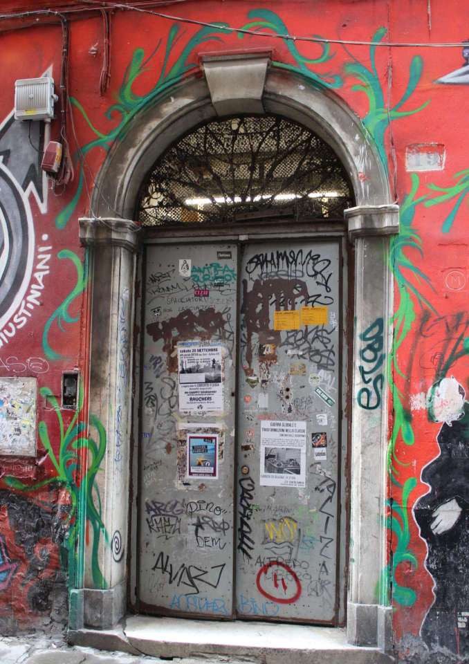 Il portale in marmo su via dei Giustiniani, con il portone ricoperto di graffiti